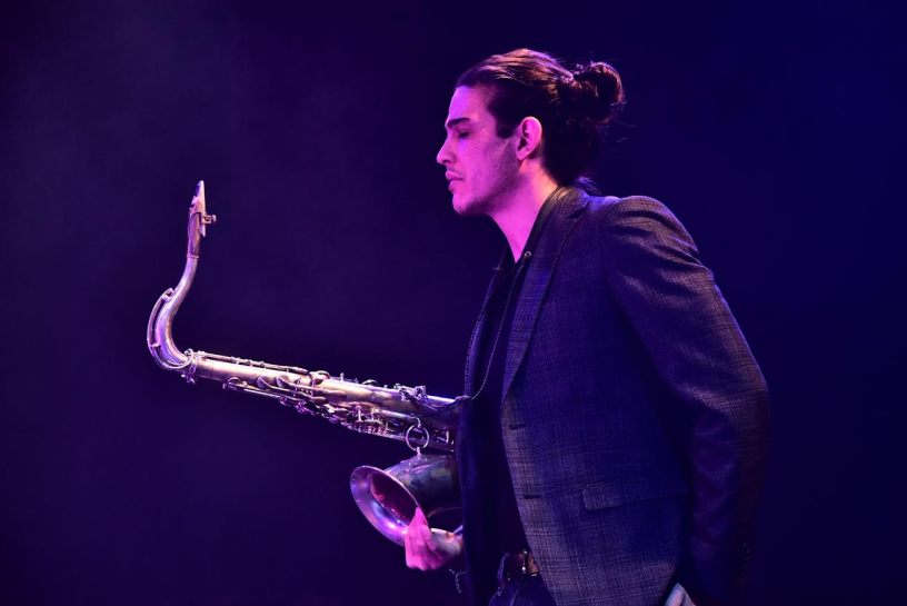 Mattia Basilico, giovane sassofonista jazz italiano, durante un'esibizione dal vivo illuminata da luci di scena viola e blu, protagonista del Monfrà Jazz Fest 2026.