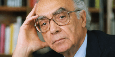 Ritratto fotografico realistico di José Saramago nel suo studio, circondato da libri, mentre riflette con sguardo intenso e pensieroso.