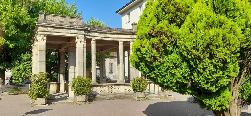 Storico padiglione monumentale nel centro di Valle San Bartolomeo ad Alessandria, circondato da alberi e aree verdi in una luminosa giornata estiva.