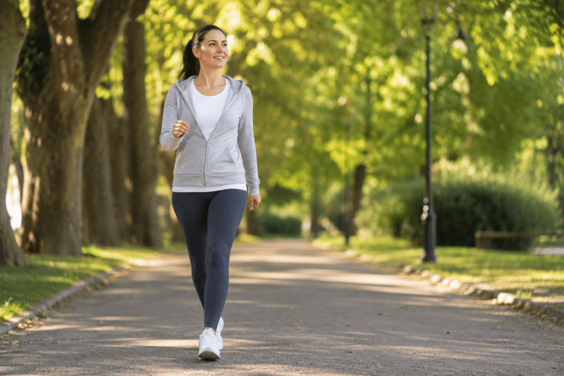 Donna che cammina con passo deciso in un parco alberato, simbolo di benessere, attività fisica quotidiana e prevenzione per la salute.