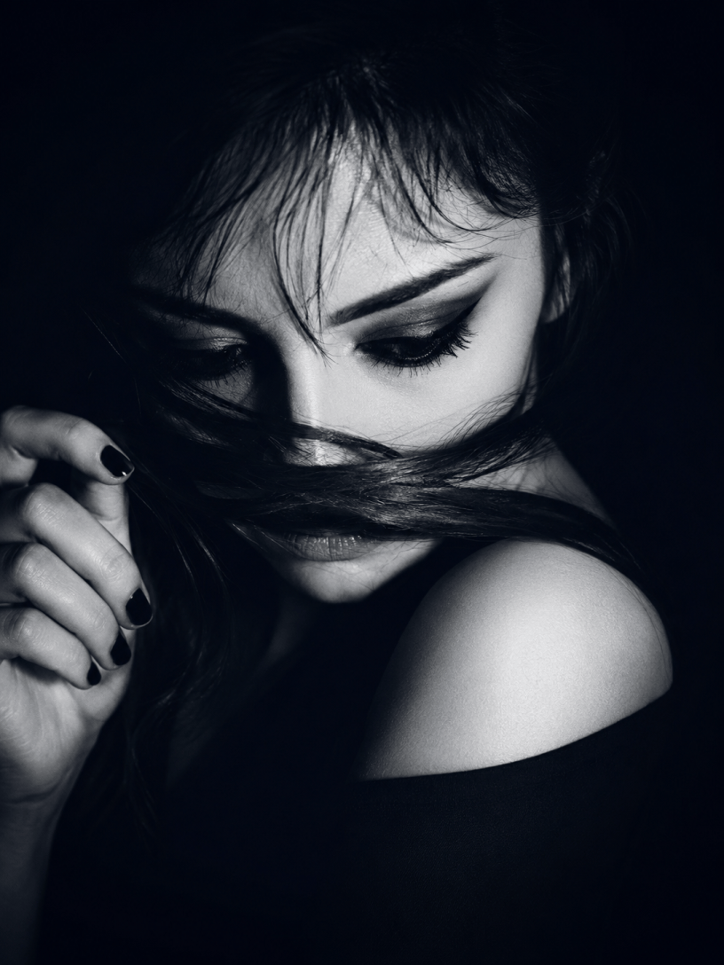 Ritratto artistico in bianco e nero di una giovane donna dai tratti intensi e malinconici, con una ciocca di capelli che attraversa il volto come un velo simbolico. L'immagine richiama introspezione, mistero e sensibilità emotiva.