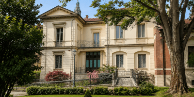 Villa Guerci ad Alessandria circondata da alberi e giardini curati, con elegante facciata storica in stile neoclassico e vista sul campanile della Cattedrale sullo sfondo.