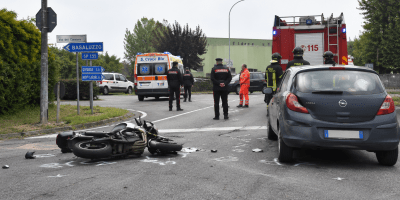 Incidente stradale tra auto e moto a un incrocio di una strada provinciale, con la presenza di mezzi di soccorso, Carabinieri e Vigili del Fuoco intervenuti sul luogo della tragedia.