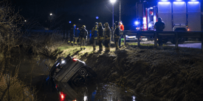 Auto finita in un canale durante la notte mentre vigili del fuoco, soccorritori e forze dell’ordine operano sul luogo dell’incidente illuminato dai lampeggianti di emergenza.