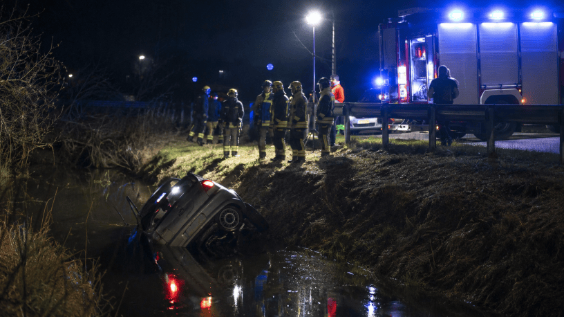 Auto finita in un canale durante la notte mentre vigili del fuoco, soccorritori e forze dell’ordine operano sul luogo dell’incidente illuminato dai lampeggianti di emergenza.