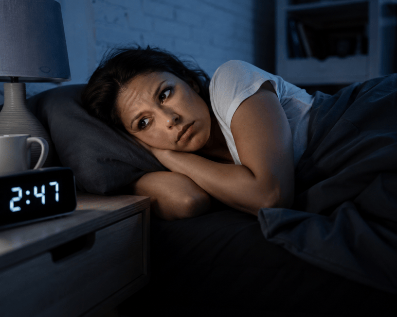 Donna sdraiata nel letto durante la notte con gli occhi aperti, illuminata dalla tenue luce di una lampada, simbolo delle difficoltà legate all'insonnia e alla mancanza di sonno.