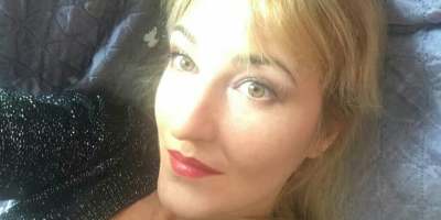 Ritratto della poetessa Nadezhda Slavova con capelli biondi e rossetto rosso, fotografata in primo piano con uno sguardo intenso e luminoso rivolto verso l'obiettivo.