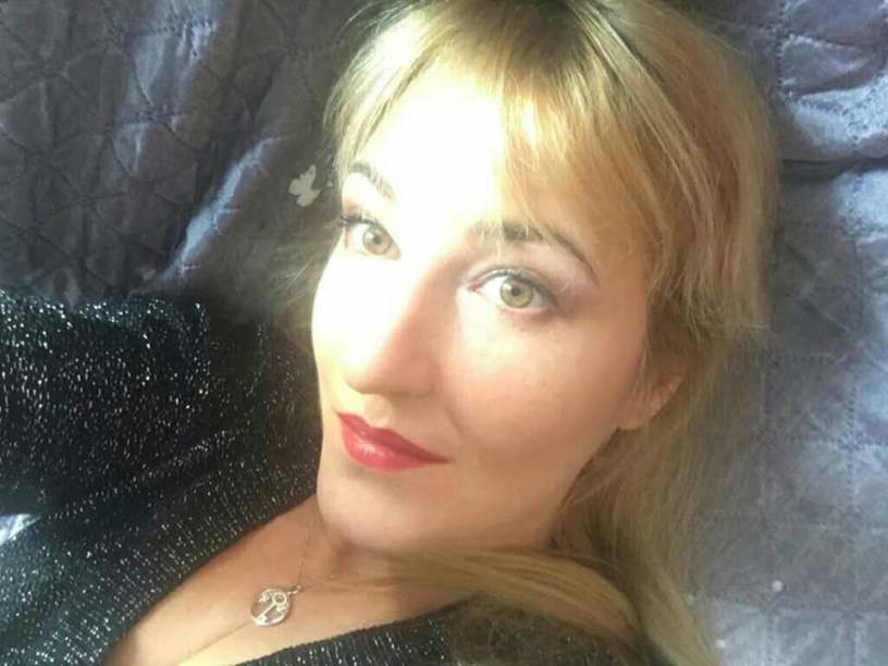 Ritratto della poetessa Nadezhda Slavova con capelli biondi e rossetto rosso, fotografata in primo piano con uno sguardo intenso e luminoso rivolto verso l'obiettivo.