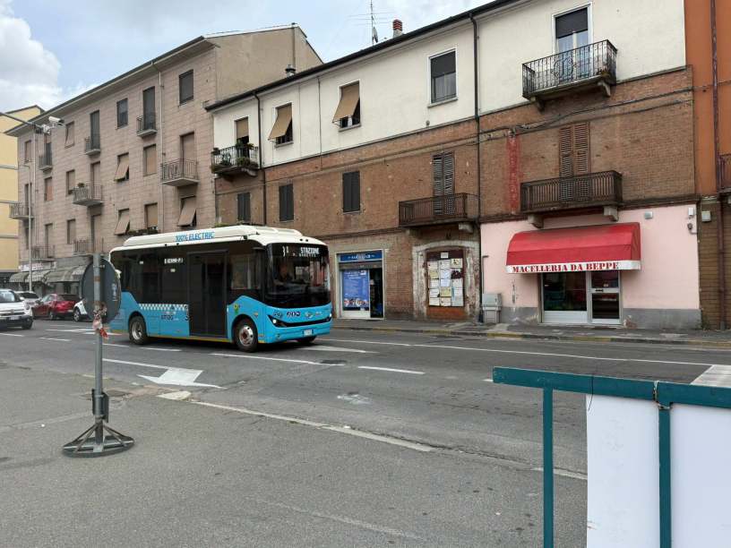 Autobus elettrico della linea urbana di Alessandria in transito lungo corso Acqui nel Quartiere Cristo, davanti alle attività commerciali e agli edifici residenziali della zona.