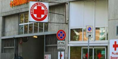 Ingresso del Pronto Soccorso dell'Ospedale Civile di Alessandria con la caratteristica insegna della croce rossa, la segnaletica stradale e l'accesso principale, simbolo delle difficoltà di accessibilità e parcheggio nell'area ospedaliera.