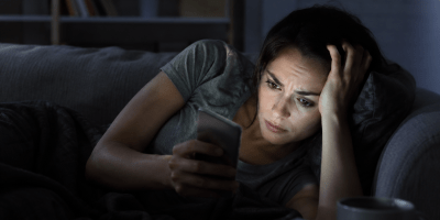 Persona che legge notizie sullo smartphone durante la notte con espressione preoccupata, simbolo dell'ansia informativa e del fenomeno del doomscrolling.