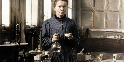 Ritratto realistico di Marie Curie nel suo laboratorio storico mentre osserva strumenti scientifici tra provette e apparecchiature utilizzate per gli studi sulla radioattività.