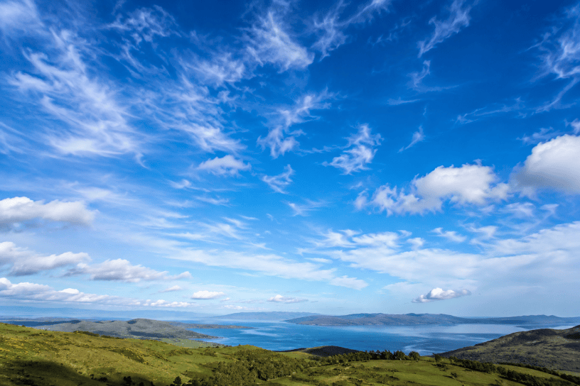 Ampio paesaggio naturale sotto un cielo azzurro attraversato da nuvole bianche, immagine che illustra il fenomeno scientifico del colore blu del cielo.