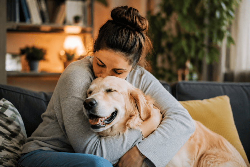 Donna che abbraccia affettuosamente il proprio cane sul divano di casa, in un ambiente accogliente e rilassante, simbolo del legame emotivo tra esseri umani e animali domestici.