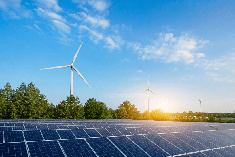 Impianto di energia rinnovabile con pannelli fotovoltaici e turbine eoliche immersi in un paesaggio naturale al tramonto, simbolo della transizione energetica sostenibile.