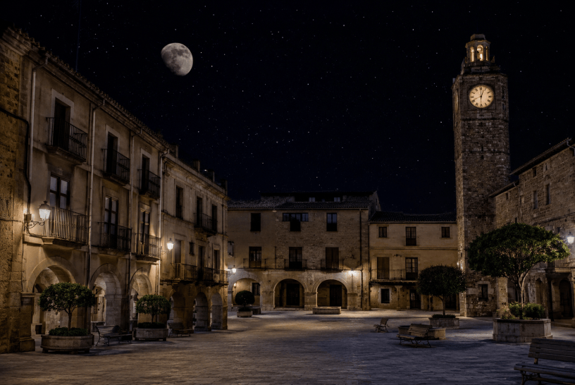 Piazza antica illuminata dalla luna in una notte estiva, con edifici storici, torre dell'orologio e atmosfera silenziosa e suggestiva ispirata alla poesia Notte d'estate di Antonio Machado.