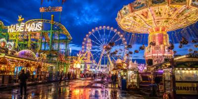 Grande Luna Park illuminato di sera con ruota panoramica, giostre colorate e luci riflesse sul pavimento bagnato, in un'atmosfera suggestiva e ricca di emozioni.