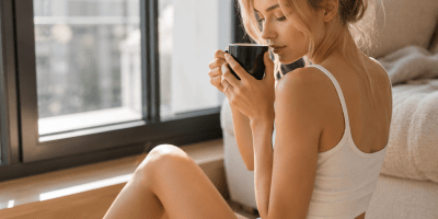 Giovane donna seduta vicino a una grande finestra mentre sorseggia una tazza di caffè in un'atmosfera rilassante e luminosa del mattino.