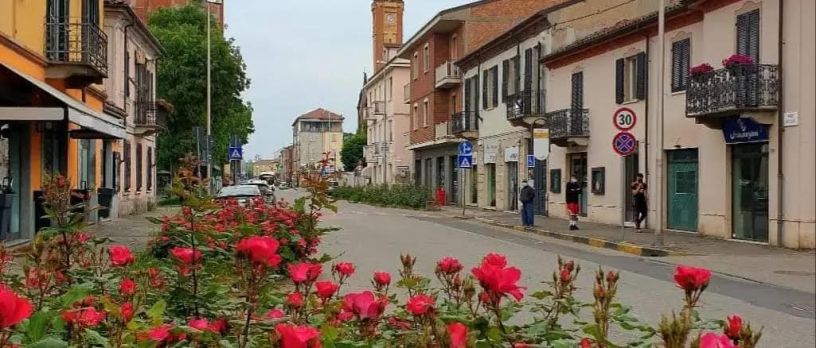 Veduta di Corso Acqui nel Quartiere Cristo di Alessandria, con aiuole fiorite in primo piano, edifici storici, attività commerciali e una delle principali arterie della zona sud della città.