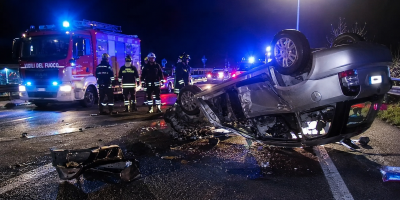 Scenario di un grave incidente stradale notturno con un'auto ribaltata, mezzi di soccorso, Vigili del Fuoco e forze dell'ordine impegnati nelle operazioni di emergenza su una strada italiana.