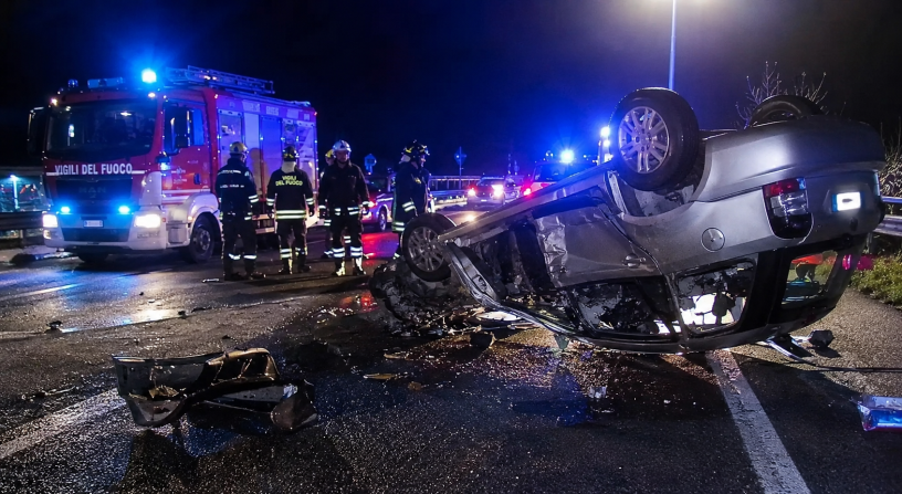 Scenario di un grave incidente stradale notturno con un'auto ribaltata, mezzi di soccorso, Vigili del Fuoco e forze dell'ordine impegnati nelle operazioni di emergenza su una strada italiana.