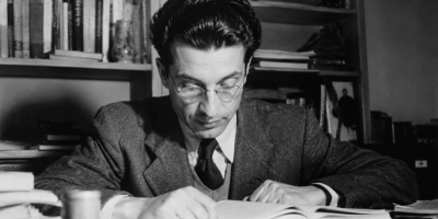 Ritratto fotografico realistico in bianco e nero di Cesare Pavese nel suo studio, circondato da libri e manoscritti, mentre legge e riflette. Immagine dedicata alla poesia Passerò per piazza di Spagna, scelta per la Maturità 2026.