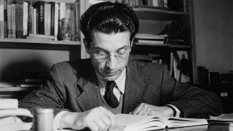 Ritratto fotografico realistico in bianco e nero di Cesare Pavese nel suo studio, circondato da libri e manoscritti, mentre legge e riflette. Immagine dedicata alla poesia Passerò per piazza di Spagna, scelta per la Maturità 2026.