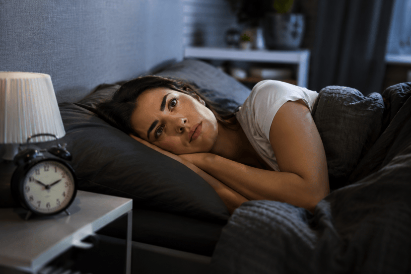 Persona sdraiata nel letto al mattino con espressione stanca e affaticata, mentre la luce dell'alba entra dalla finestra della camera da letto.