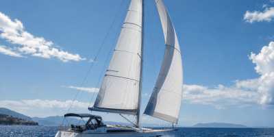 Elegante barca a vela bianca che naviga nel mare blu sotto un cielo estivo luminoso. Le vele gonfiate dal vento dominano la scena, evocando libertà, viaggio e armonia con la natura.