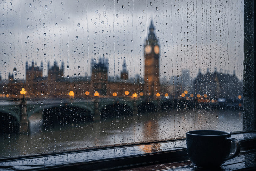 Gocce di pioggia su una finestra affacciata su una città avvolta dalla foschia, immagine evocativa ispirata alla poesia The Rain di William Ernest Henley.