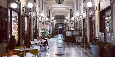 Interno della storica Galleria Guerci di Alessandria con elegante pavimentazione a scacchi, illuminazione d'epoca, vetrine commerciali e tavolini dei locali presenti nel celebre passaggio coperto del centro storico cittadino.