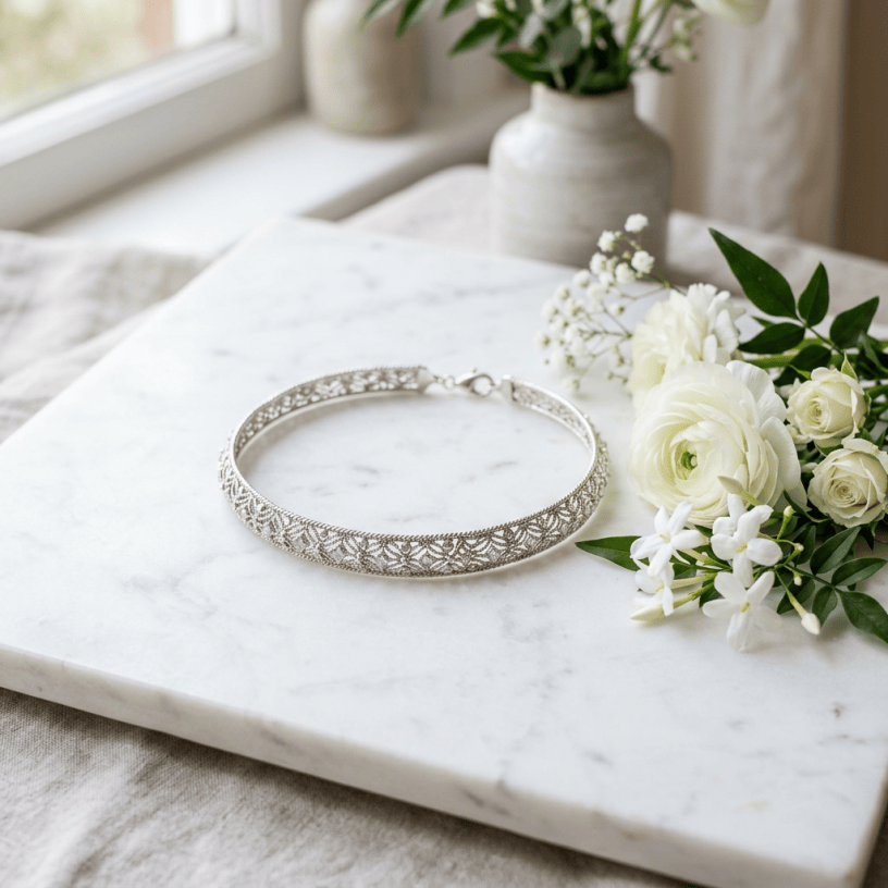 Silver filigree bracelet with intricate patterns placed on a marble slab next to white flowers
