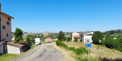 Panorama delle colline del Monferrato con vista su Lu Monferrato all'orizzonte, tra campi coltivati, vigneti e strade di campagna immerse nel verde.