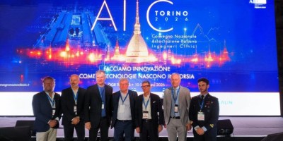 Partecipanti e relatori del 26° Convegno Nazionale AIIC fotografati sul palco a Torino davanti al grande schermo dedicato all'innovazione tecnologica e all'ingegneria clinica applicata alla sanità e alla ricerca aerospaziale.
