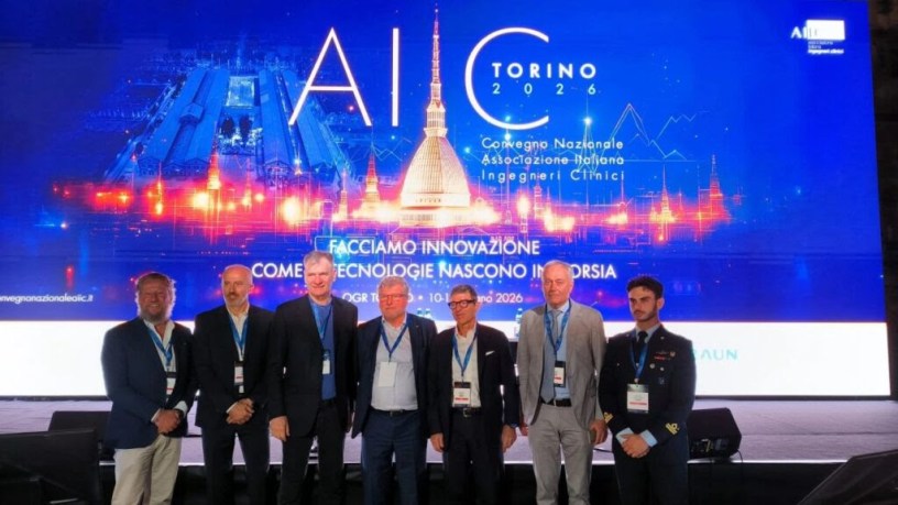 Partecipanti e relatori del 26° Convegno Nazionale AIIC fotografati sul palco a Torino davanti al grande schermo dedicato all'innovazione tecnologica e all'ingegneria clinica applicata alla sanità e alla ricerca aerospaziale.