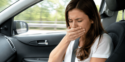Persona seduta sul sedile del passeggero che manifesta sintomi di mal d'auto durante un viaggio, con espressione di nausea, a rappresentare la cinetosi e il conflitto tra cervello e sistema vestibolare.