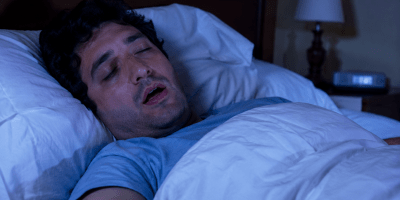 Persona che parla nel sonno mentre dorme serenamente nel proprio letto, immagine illustrativa della somniloquia e dei fenomeni studiati dalla medicina del sonno.