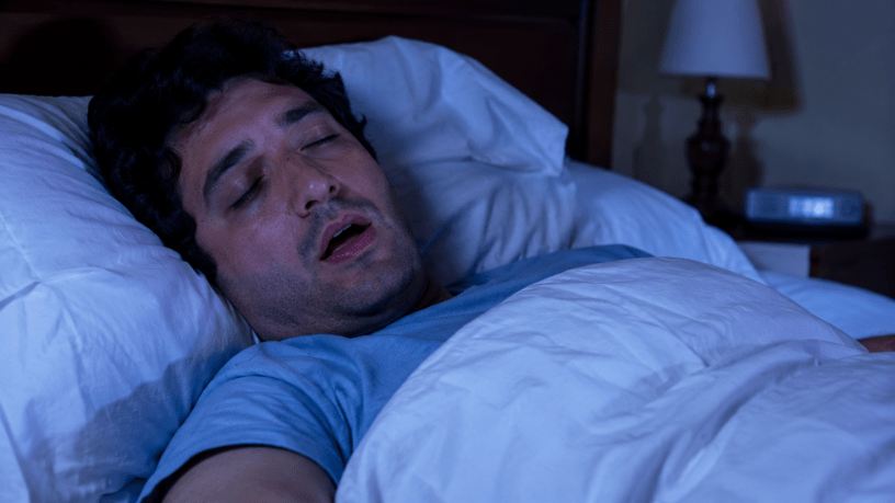Persona che parla nel sonno mentre dorme serenamente nel proprio letto, immagine illustrativa della somniloquia e dei fenomeni studiati dalla medicina del sonno.