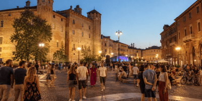 Veduta del Complesso Conventuale di San Francesco ad Alessandria con cittadini che partecipano a un evento estivo in un'atmosfera di socialità e valorizzazione del patrimonio storico.