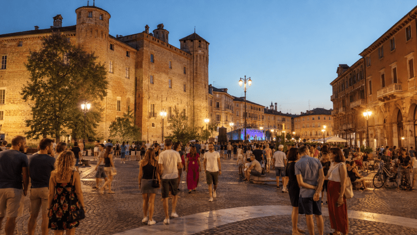 Veduta del Complesso Conventuale di San Francesco ad Alessandria con cittadini che partecipano a un evento estivo in un'atmosfera di socialità e valorizzazione del patrimonio storico.