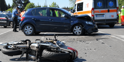 Motocicletta a terra dopo lo scontro con un’automobile, mentre ambulanza del 118 e forze dell’ordine intervengono sul luogo dell’incidente.