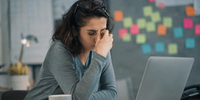 Donna seduta davanti al computer con espressione affaticata e concentrata, simbolo della nebbia mentale (brain fog), delle difficoltà di memoria e della riduzione della concentrazione in un ambiente di lavoro.