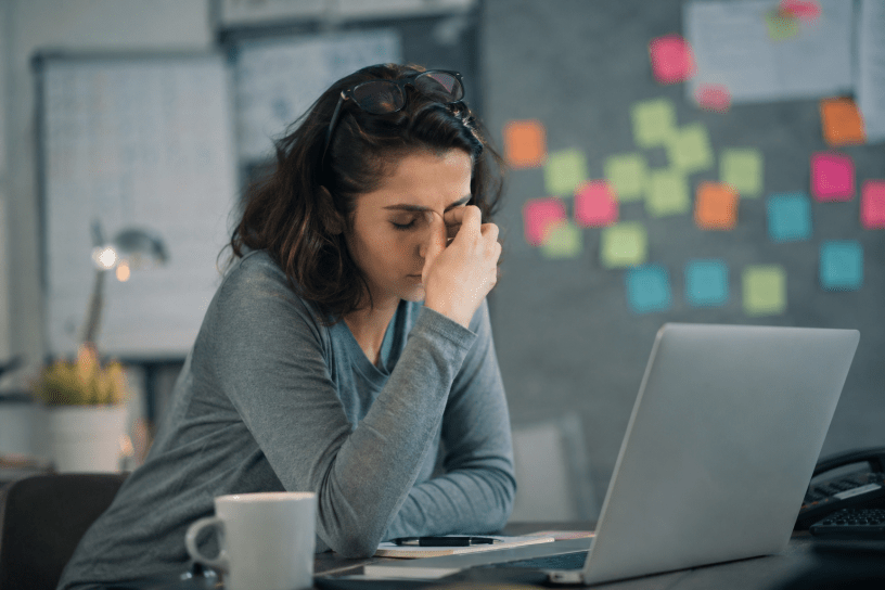 Donna seduta davanti al computer con espressione affaticata e concentrata, simbolo della nebbia mentale (brain fog), delle difficoltà di memoria e della riduzione della concentrazione in un ambiente di lavoro.