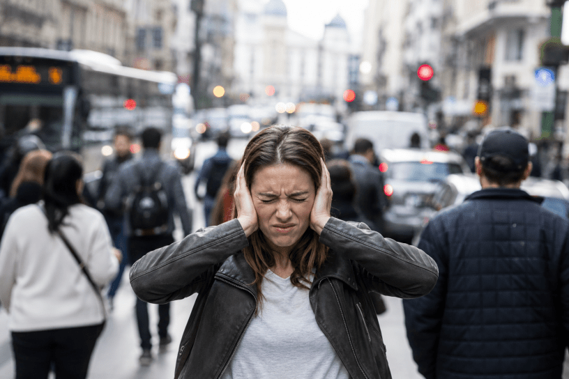 Persona in una strada cittadina molto rumorosa mentre si copre le orecchie, a rappresentare l'influenza del rumore sulla percezione del tempo secondo gli studi neuroscientifici.