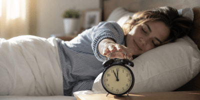 Persona che si sveglia serenamente pochi istanti prima che la sveglia suoni, in una luminosa camera da letto, simbolo del funzionamento dell'orologio biologico e dei ritmi circadiani.