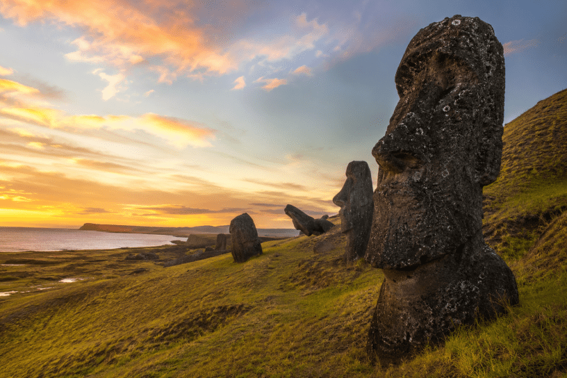 Veduta panoramica dell'Isola di Pasqua al tramonto con alcuni Moai in primo piano affacciati sull'oceano, simbolo del rapporto tra uomo, ambiente e sostenibilità. Immagine illustrativa realizzata con intelligenza artificiale.