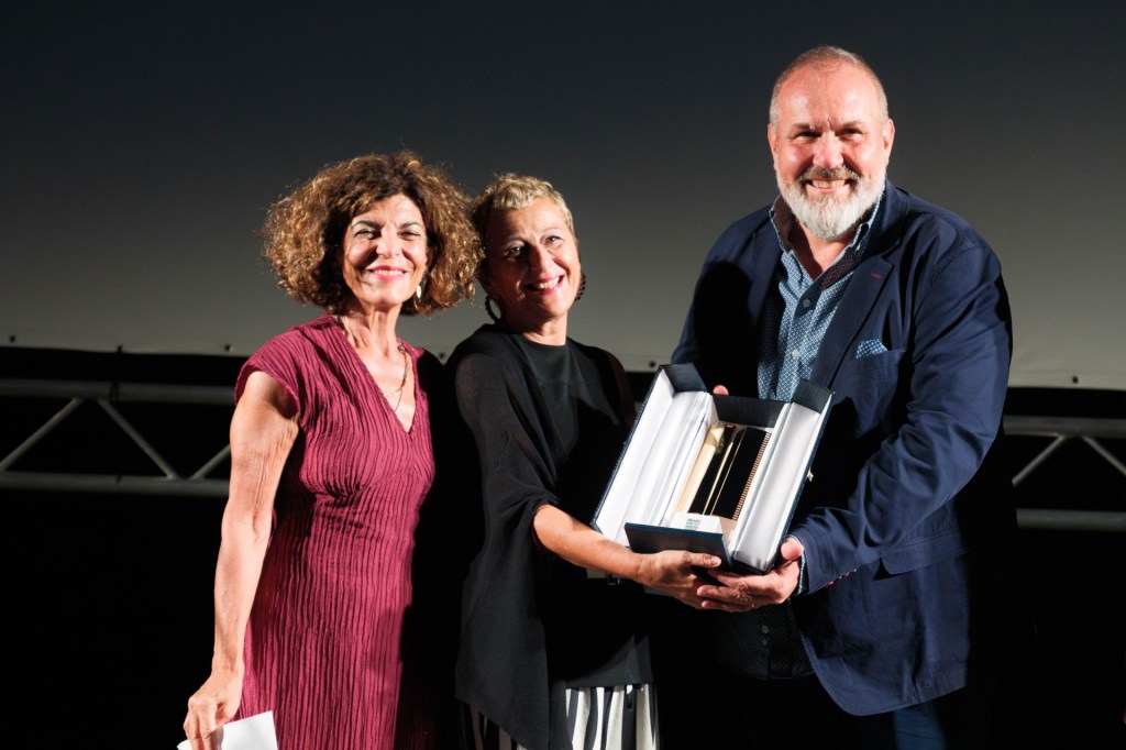 Three individuals standing together on stage, smiling. One person is holding an award or trophy, while the others look on with excitement.