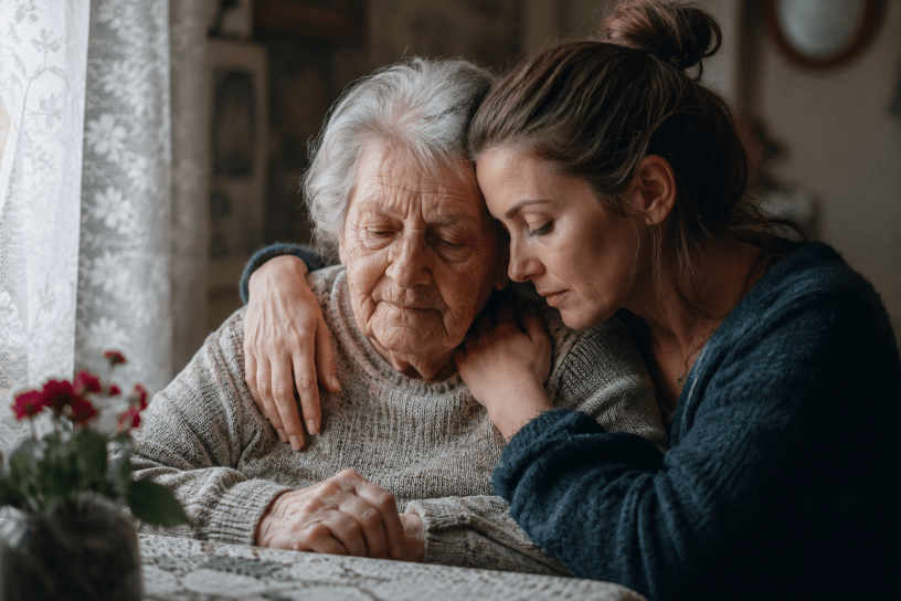 Una figlia abbraccia con tenerezza la madre anziana affetta da Alzheimer in un momento di profondo affetto e vicinanza, all'interno di una stanza illuminata dalla luce naturale.