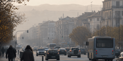 Strada urbana trafficata avvolta da una leggera foschia, con automobili, autobus e palazzi sullo sfondo, immagine simbolica dell’inquinamento atmosferico nelle città piemontesi.