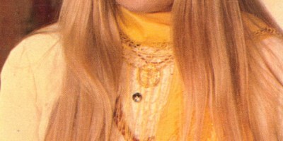 Ritratto di Gabriella Ferri nel 1975, con lunghi capelli biondi, abito chiaro e sciarpa gialla.